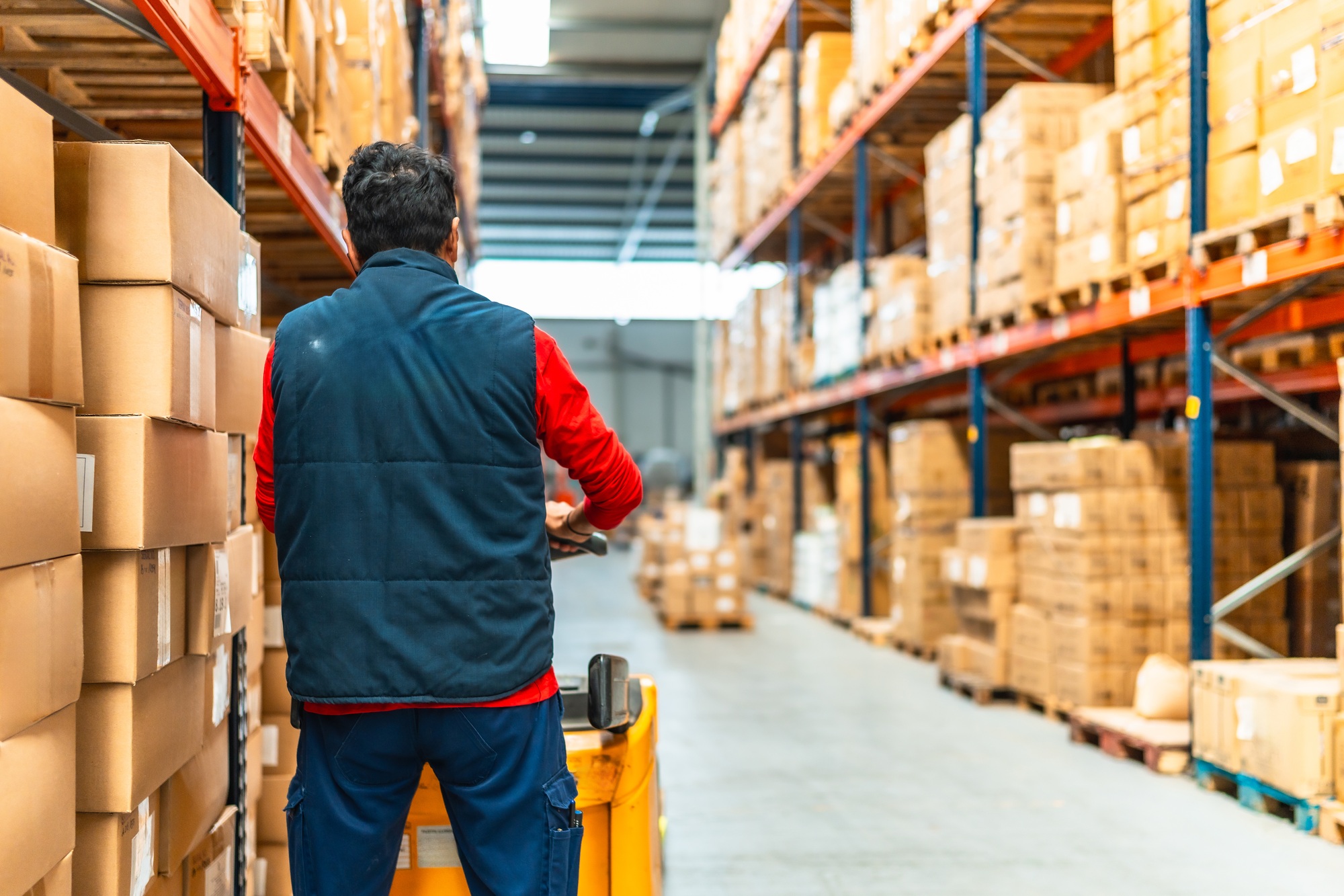 Latin worker with machinery in the logistics warehouse